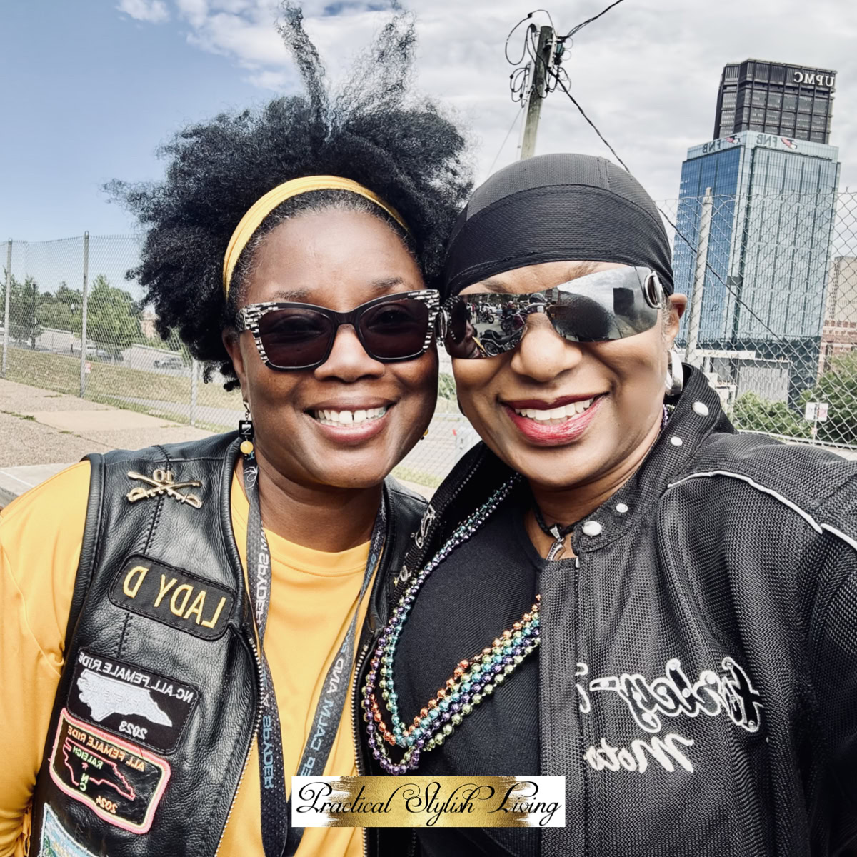 Two women of color smiling, with the left person wearing a black motorcycle vest decorated with patches including "LADY D" and a North Carolina emblem.